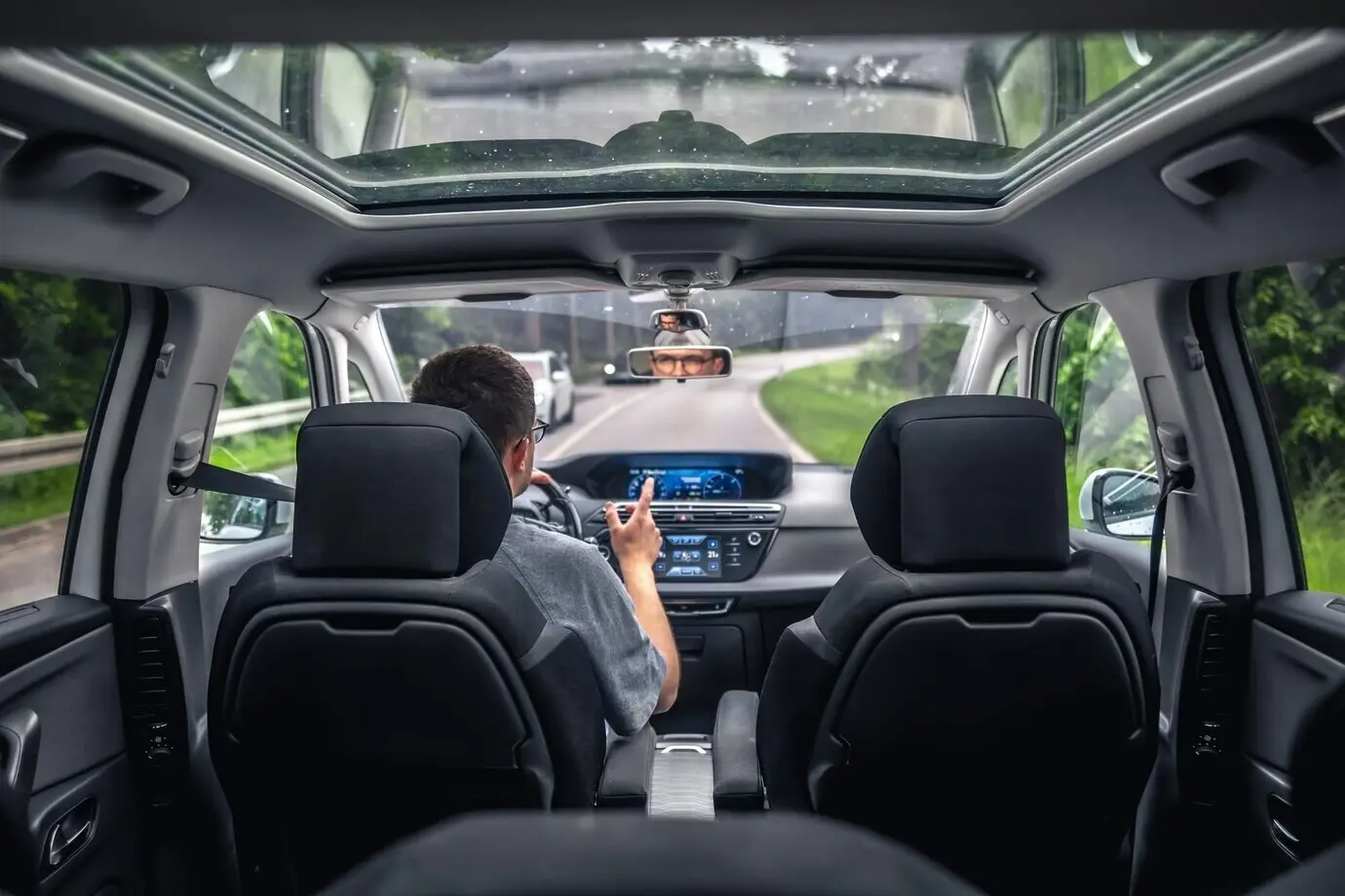 Ein Fahrer auf einer Waldstraße in einem modernen Auto, der gestikuliert.
